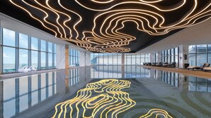 A modern indoor swimming pool with a reflective floor and a ceiling with wavy light patterns. - Renaissance Changzhou Wujin Hotel (Changzhou)