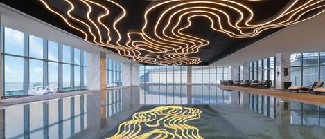 Una piscina interior moderna con suelo reflectante y techo con patrones de luz ondulados.