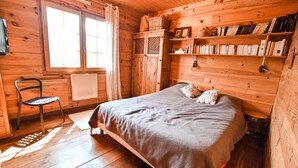 Une pièce de cabane en bois comprenant un lit, une chaise, une fenêtre et une bibliothèque.