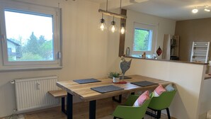 Un coin repas avec une table en bois, des chaises vertes et un coq décoratif.