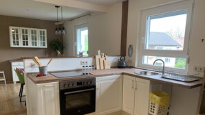 Une cuisine moderne avec des meubles blancs, un four encastré, un évier et une fenêtre qui laisse entrer la lumière naturelle.