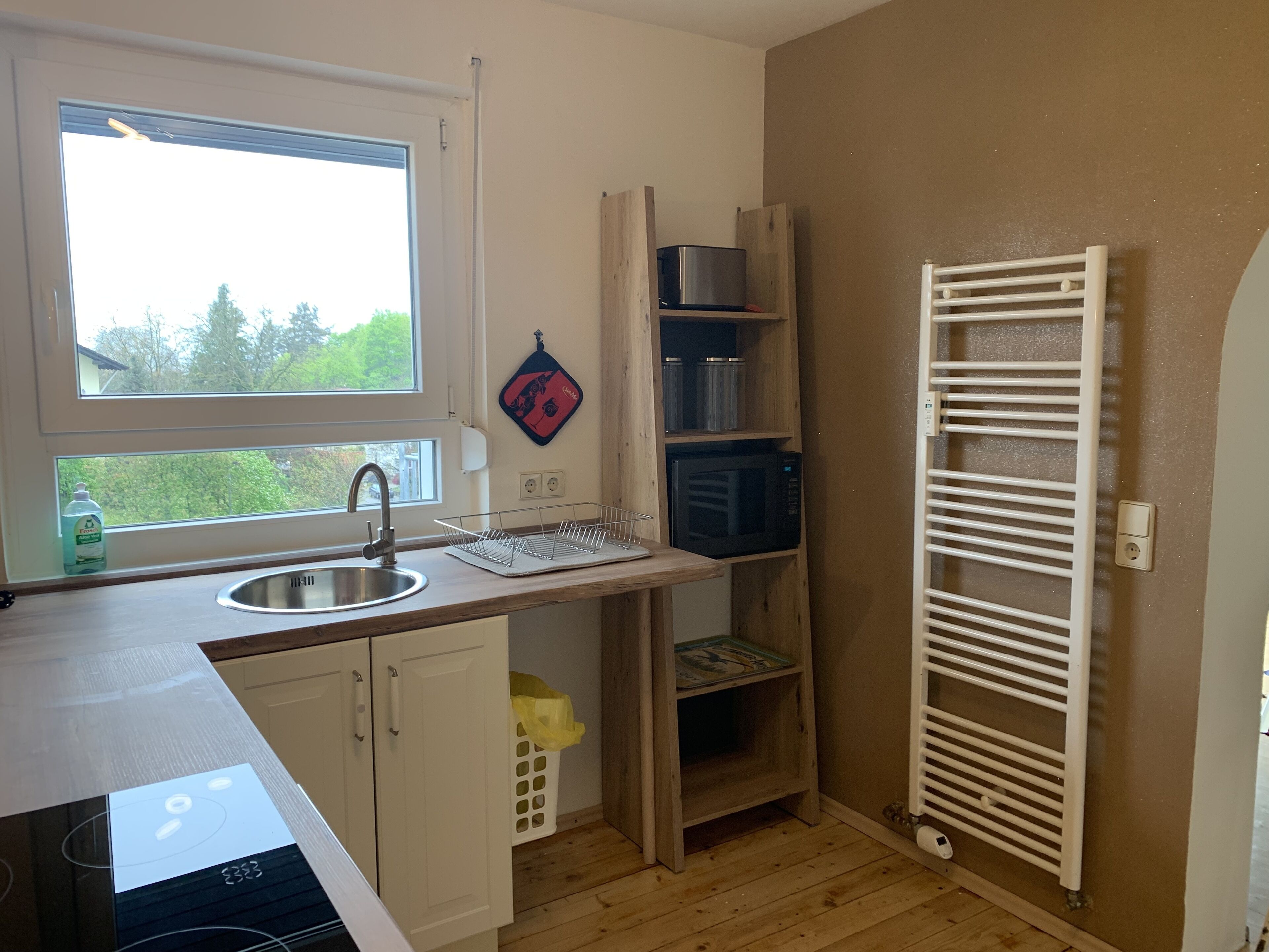Una cucina compatta con lavandino, forno a microonde e forno integrato. Una finestra offre luce naturale e vista sul verde.