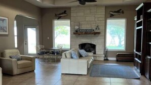 A spacious living room with a fireplace, a ceiling fan, and a large window. - Spacious 4 br getaway. Riviera Beach / Baffin Bay (Riviera)