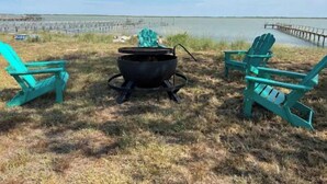 A camping setup with a black portable stove and two turquoise Adirondack chairs by a lake. - Spacious 4 br getaway. Riviera Beach / Baffin Bay (Riviera)