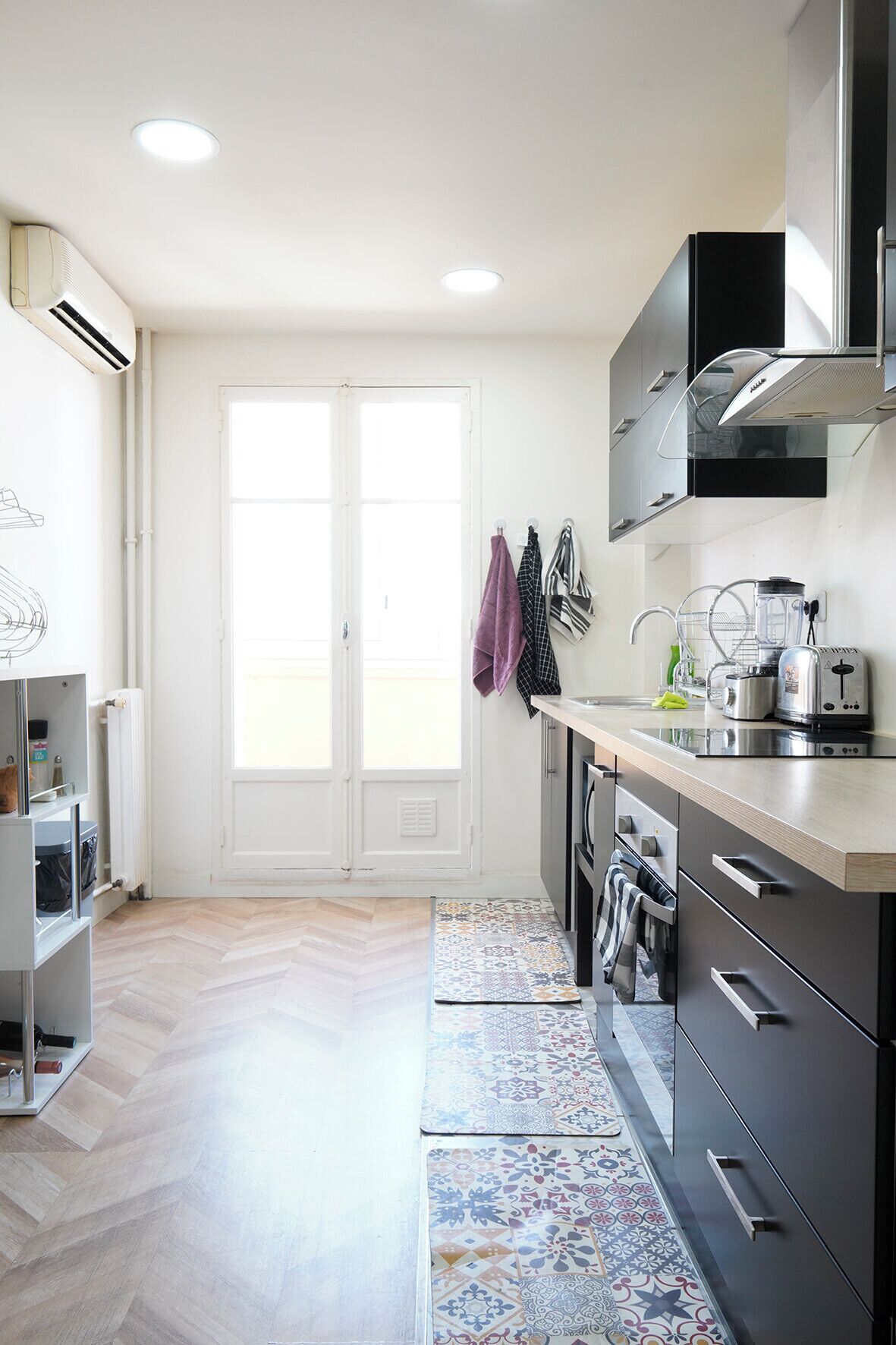 Une cuisine moderne avec un sol décoré d’un motif en chevrons, un four encastré et une hotte en acier inoxydable.