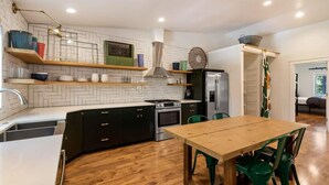 Una cocina moderna con baldosas blancas tipo espiga, armarios negros, una mesa de comedor de madera y sillas verdes.
