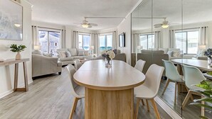 A modern hotel room with a large dining table, a sofa set, a TV, and a balcony with a view. - Oceanfront Balcony Views, Pool,  STEPS to Beach, Restaurants, Shops (Wrightsville Beach)