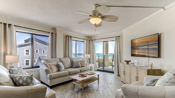 A modern living room with a sofa, coffee table, and a ceiling fan. - Oceanfront Balcony Views, Pool,  STEPS to Beach, Restaurants, Shops (Wrightsville Beach)