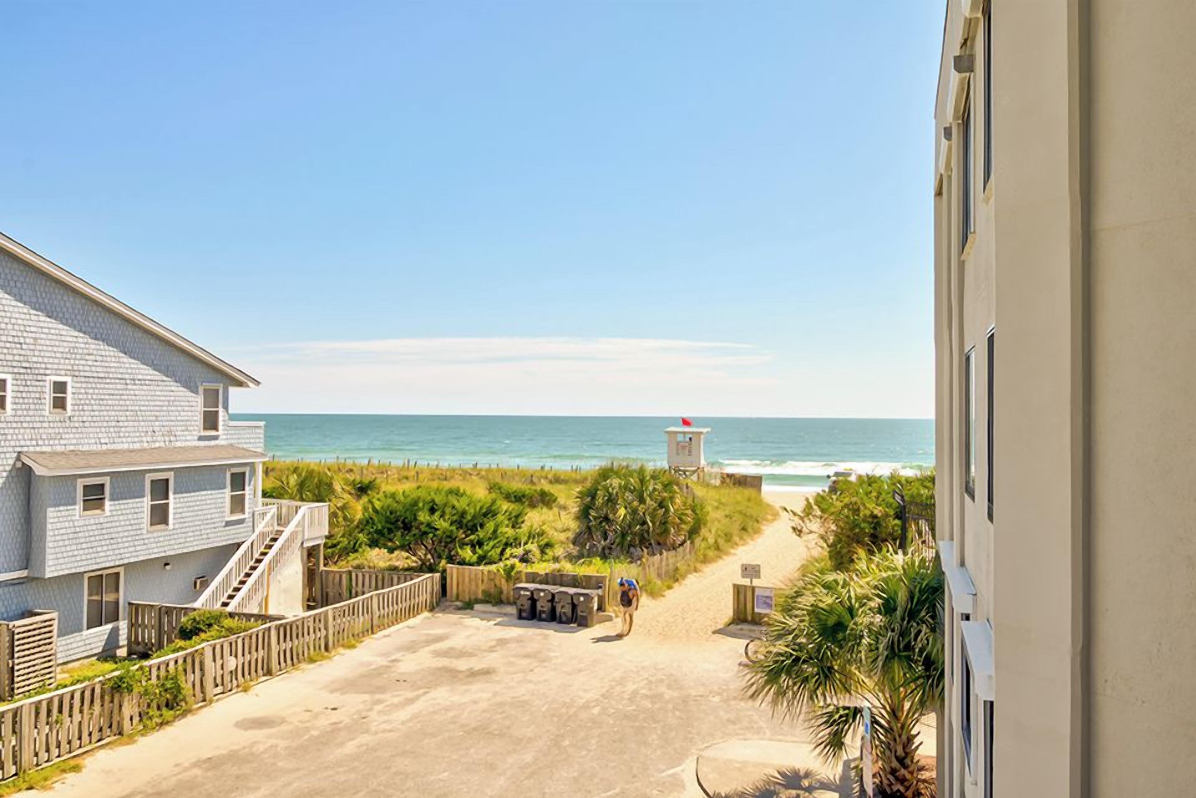 A beachfront property with a wooden fence, a pathway leading to the beach, and a lifeguard tower in the distance.