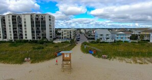 Une vue sur la plage avec un poste de surveillance des sauveteurs, un sentier sablonneux et des immeubles résidentiels en arrière-plan.