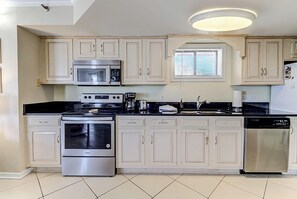 A modern kitchen with stainless steel appliances, white cabinetry, and a central island. - Ocean Views, Balcony, Pool, STEPS to Beach Restaurants Shops (Wrightsville Beach)