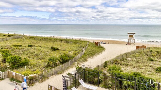 A beach view with a wooden fence, a lifeguard tower, and a sandy path leading to the water. - Ocean Views, Balcony, Pool,  STEPS to Beach Restaurants Shops (Wrightsville Beach)