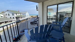 A balcony with blue Adirondack chairs, a glass door, and a view of houses and the ocean. - Ocean Views, Balcony, Pool,  STEPS to Beach Restaurants Shops (Wrightsville Beach)