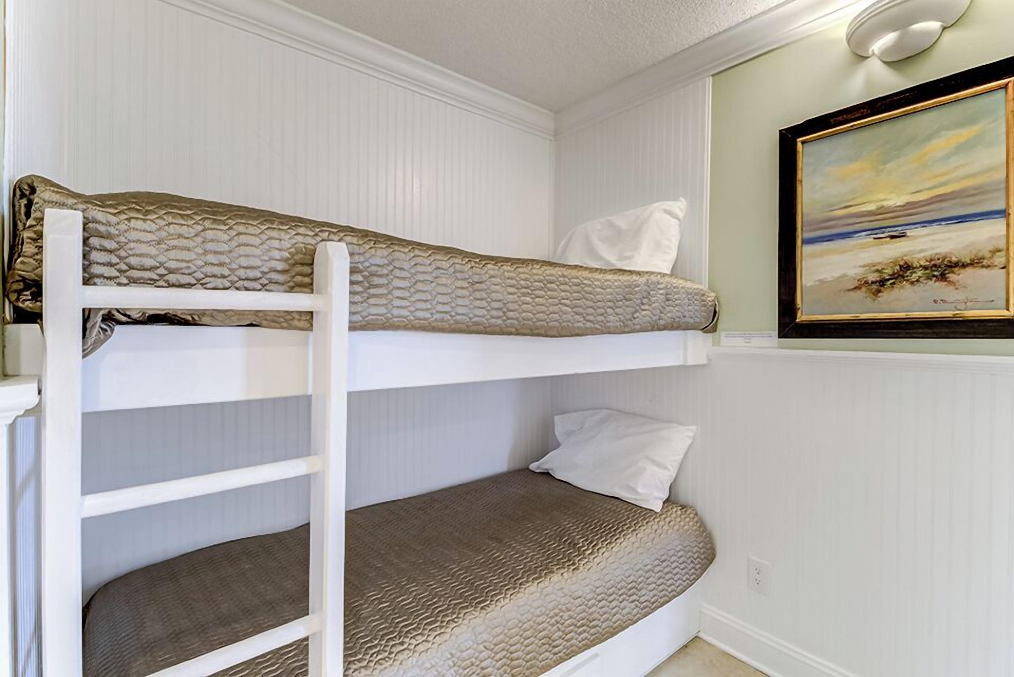 A bunk bed with a white headboard, a lower bunk with a brown mattress, and a painting of a beach scene on the wall.
