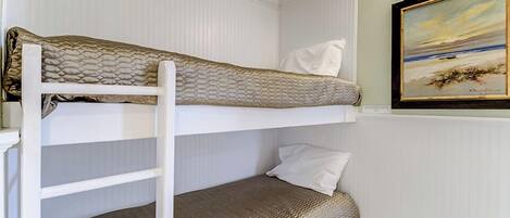 A bunk bed with a white headboard, a lower bunk with a brown mattress, and a painting of a beach scene on the wall.