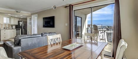 Amplia sala de estar con una mesa de comedor de madera, sillas blancas, un sofá gris y un ventilador de techo.