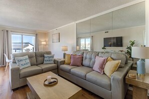 A modern living room with a sofa set, a coffee table, and a large mirror. - Ocean Views, Balcony, Pool, STEPS to Beach, Restaurants, Shops (Wrightsville Beach)