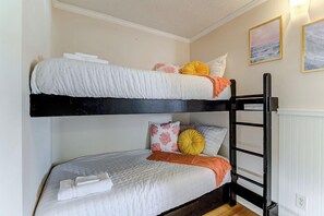 Ein Etagenbett mit einer weißen und orangefarbenen Decke, einem Kopfkissen mit Blumenmuster und einem gelben Kissen.