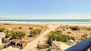 Blick auf einen Strand mit einem Weg, der zu einem Gebäude mit Außenbestuhlung und einem eingezäunten Bereich führt.