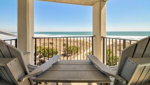 Ein Balkon mit zwei Stühlen und einem Tisch mit Blick auf einen Strand.