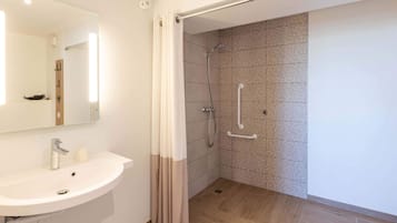 A bathroom with a sink, mirror, shower, and tiled walls.