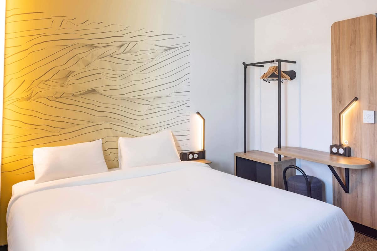 A hotel room with a large bed, bedside tables, a wooden panel wall, and a hanging coat rack.
