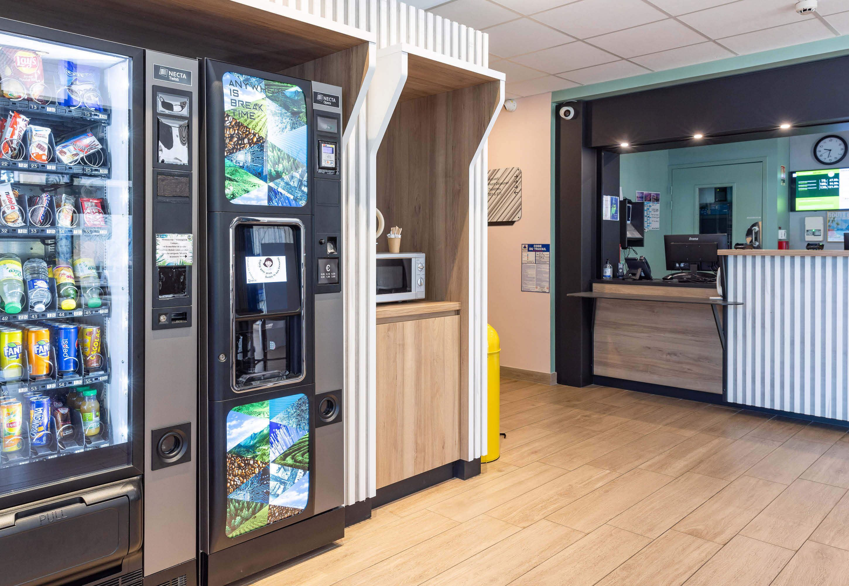 Un espace d’accueil moderne avec un comptoir en bois, un écran numérique et des distributeurs automatiques.