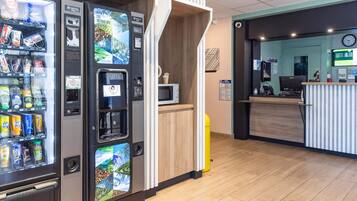 Un espace d’accueil moderne avec un comptoir en bois, un écran numérique et des distributeurs automatiques.