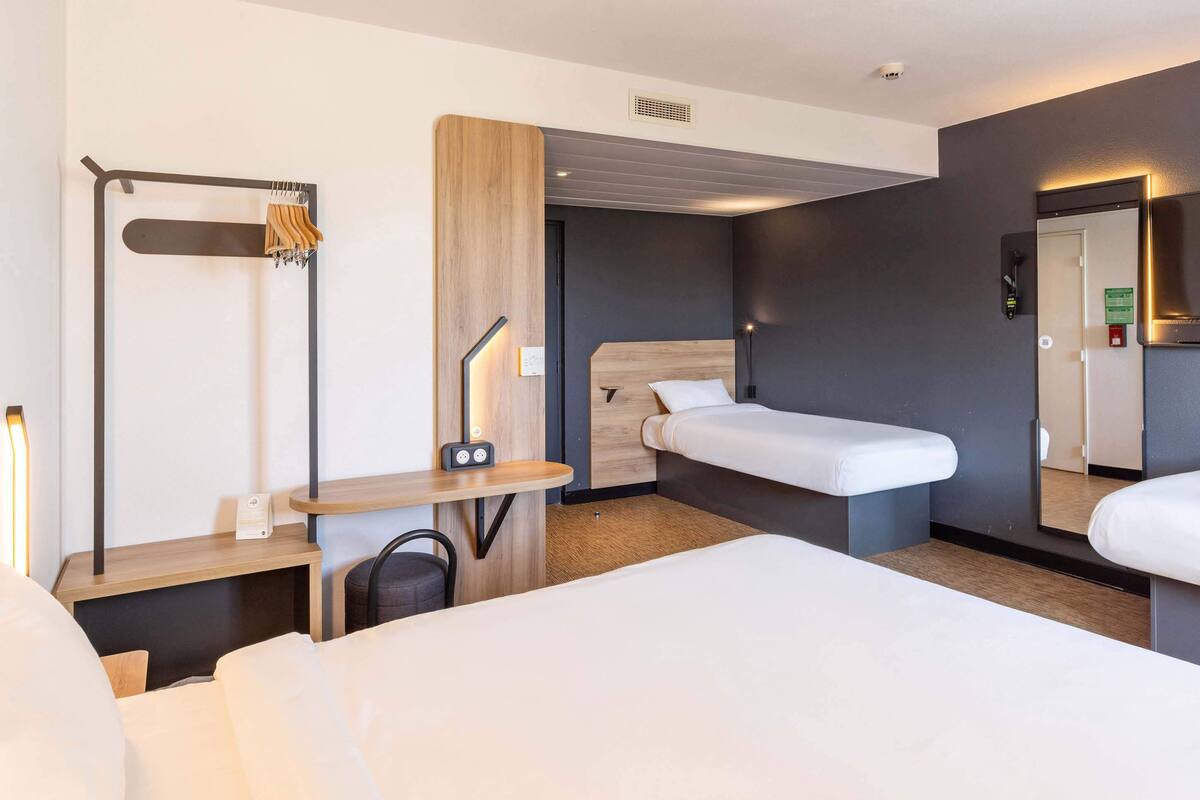 A modern hotel room with a large bed, a desk with a chair, a wardrobe, and a mirror.