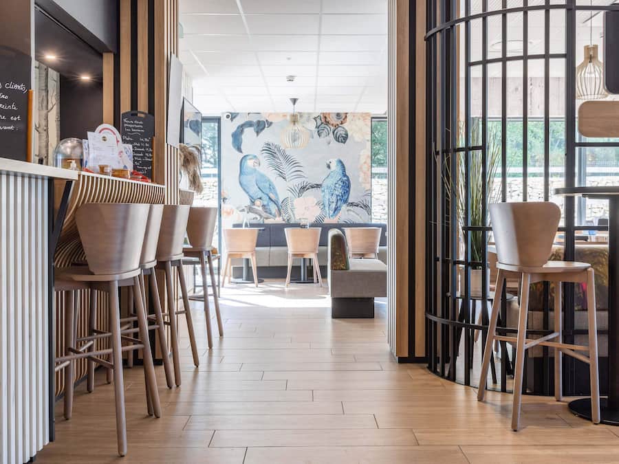 A modern cafe interior with wooden flooring, a mural of parrots, and a counter with a menu.