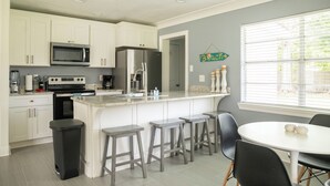 A modern kitchen with white cabinets, a stainless steel refrigerator, a microwave, and a large island with bar stools.