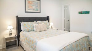 A bedroom with a bed, two bedside tables, a nightstand, a framed picture on the wall, and a door.