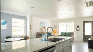 A kitchen with a large island, built-in dishwasher, and a sink. There is a dining table and chairs in the adjacent area.