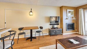 Una sala de estar con piso de madera, una mesa de comedor con sillas, un televisor, una chimenea y una mesa de centro.