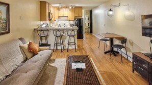 Un espacio habitable compacto con kitchenette, un sofá, zona de comedor y televisor.