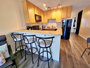 A modern kitchen with wooden cabinets, a central island with bar stools, a built-in oven, and a black refrigerator.