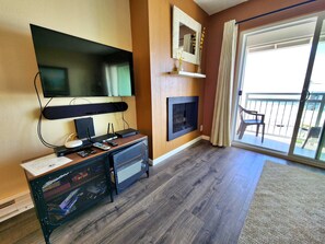 A living room with a flat-screen TV, a fireplace, and a balcony with a chair.