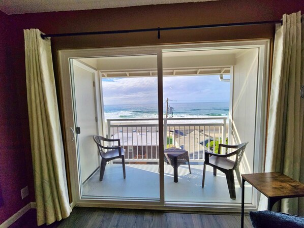A balcony with a view of the ocean, two chairs, and a small table.