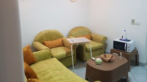 Ein Wohnzimmer mit zwei grünen Sofas, einem kleinen Tisch, einer Mikrowelle und einer Wandleuchte.