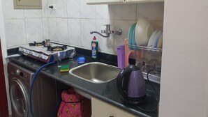 Eine kleine Küche mit Gaskochfeld, Spüle, Geschirrgestell und Wasserkocher.