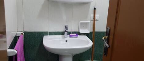 A bathroom with a white sink, green tiles, a mirror, and a mop.