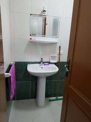 A bathroom with a white sink, green tiles, a mirror, and a mop. - One bedroom studio in Delta Sharm Resort (South Sinai Governorate)