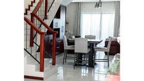 A modern living room with a wooden staircase, a dining area with a table and chairs, and a kitchen in the background. - Grayville Apartments #7 (Lusaka)