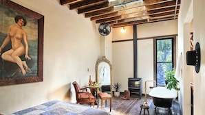 A bedroom with a large bed, a sitting area with a chair and table, a black bathtub, and a large window with a view of trees. - Western Hotel Ouray (Ouray)