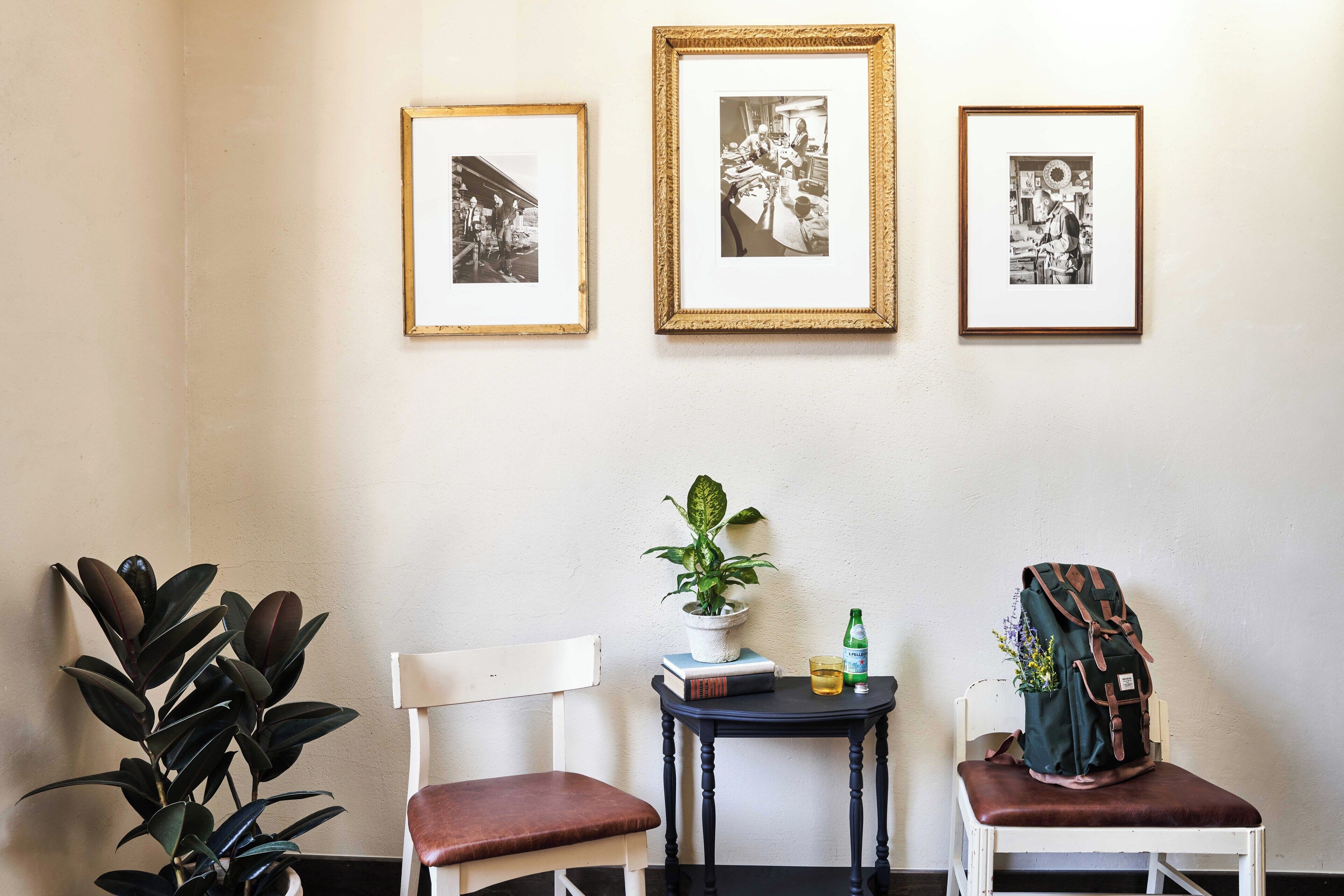 A room with three framed black and white photographs on the wall, a potted plant on a small table, and a backpack on a chair.