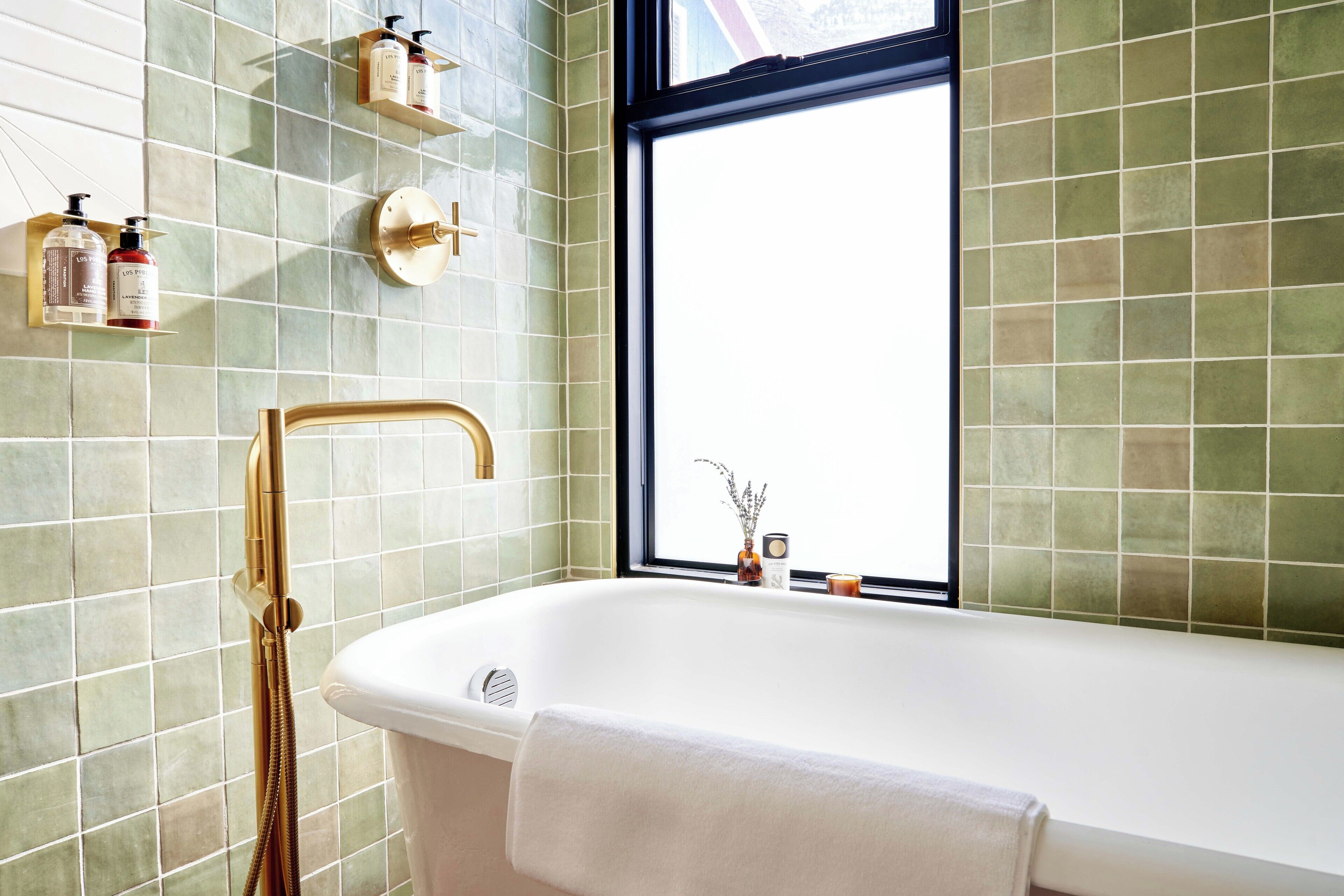 A bathroom with a freestanding bathtub, a window, and a shower with a gold faucet.