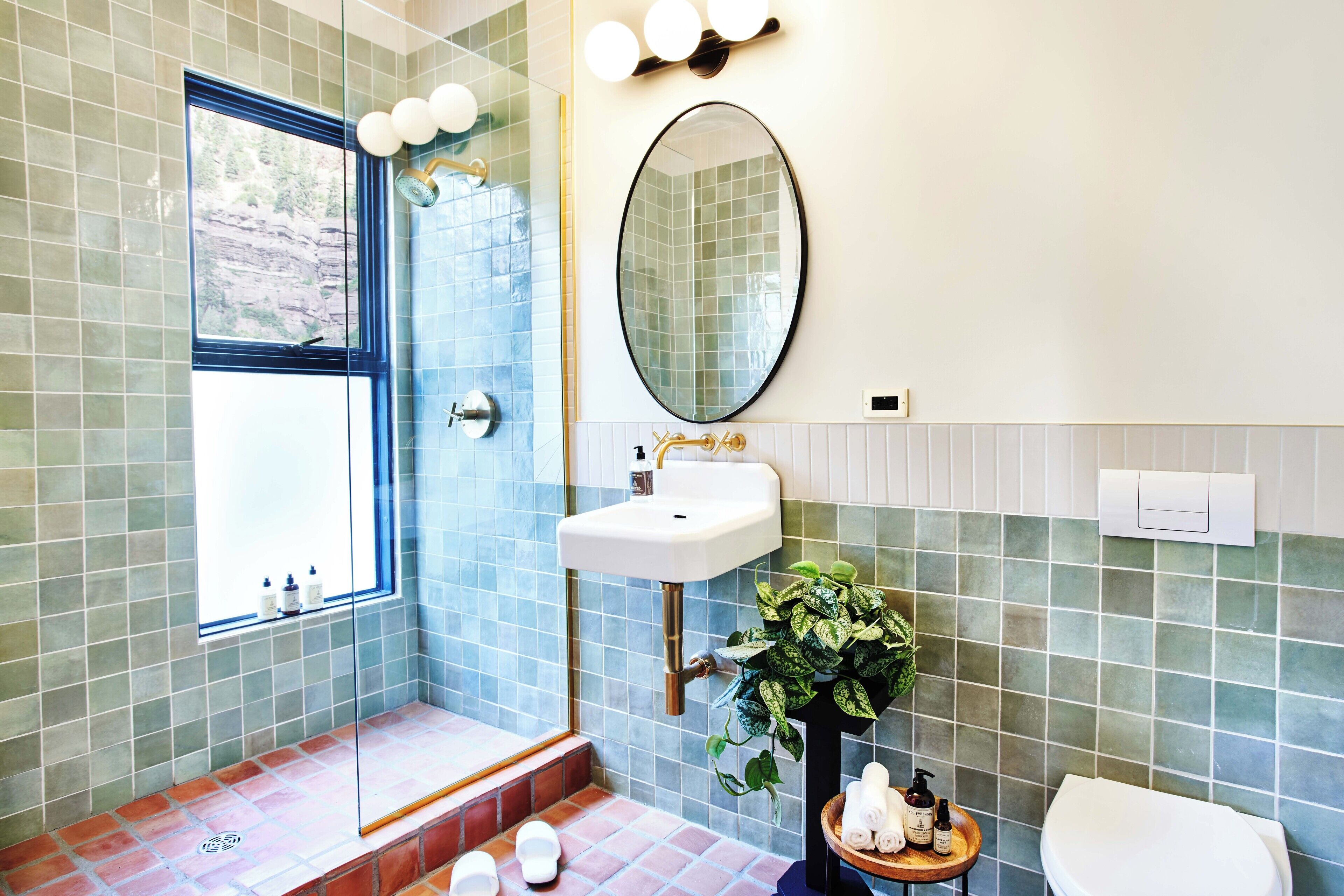 A bathroom with a shower, sink, toilet, and a window with a view of a rocky landscape.