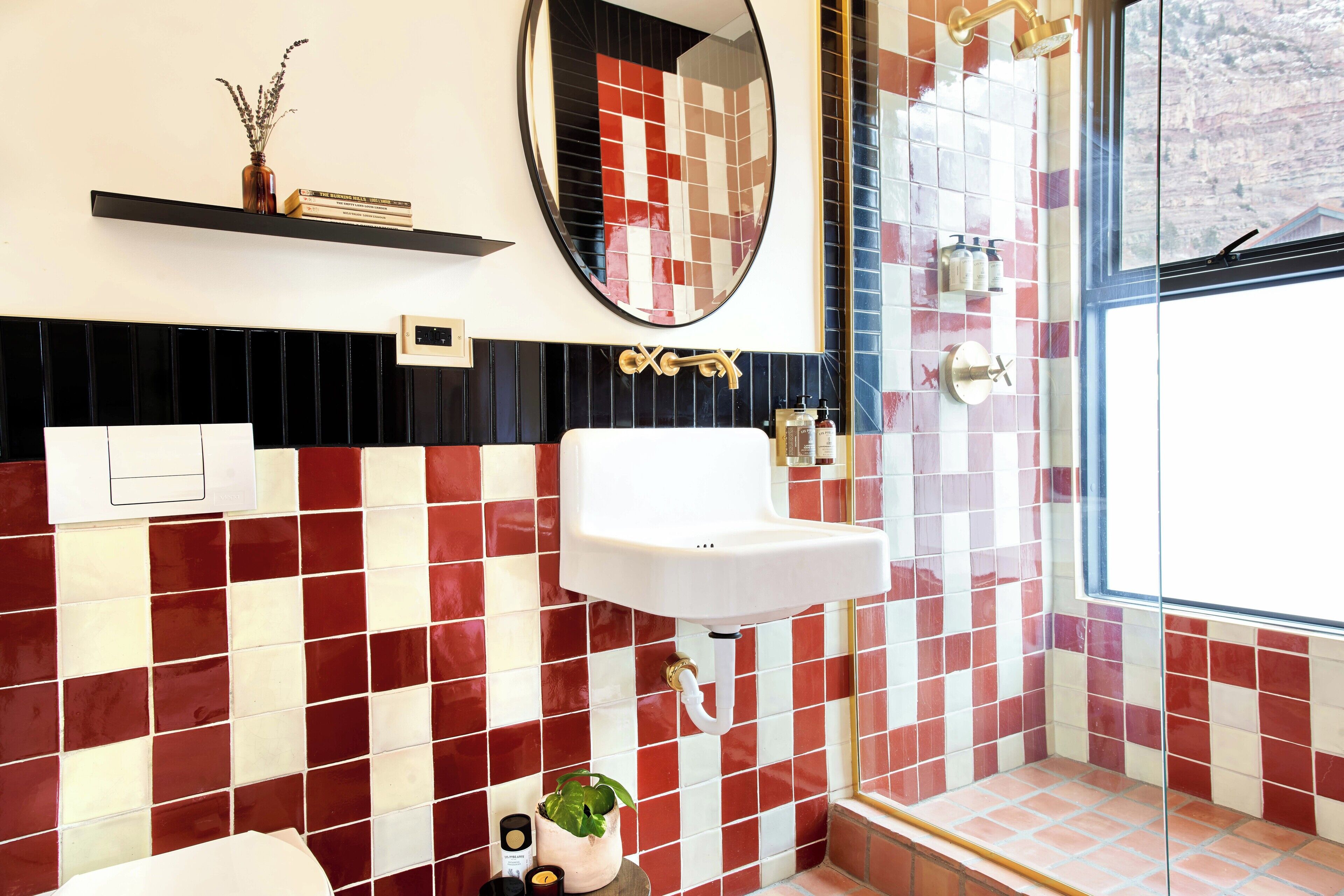 Un baño con un lavamanos blanco, paredes con azulejos blancos y rojos, un espejo y una ventana con vistas.