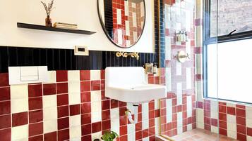 Un baño con un lavamanos blanco, paredes con azulejos blancos y rojos, un espejo y una ventana con vistas.