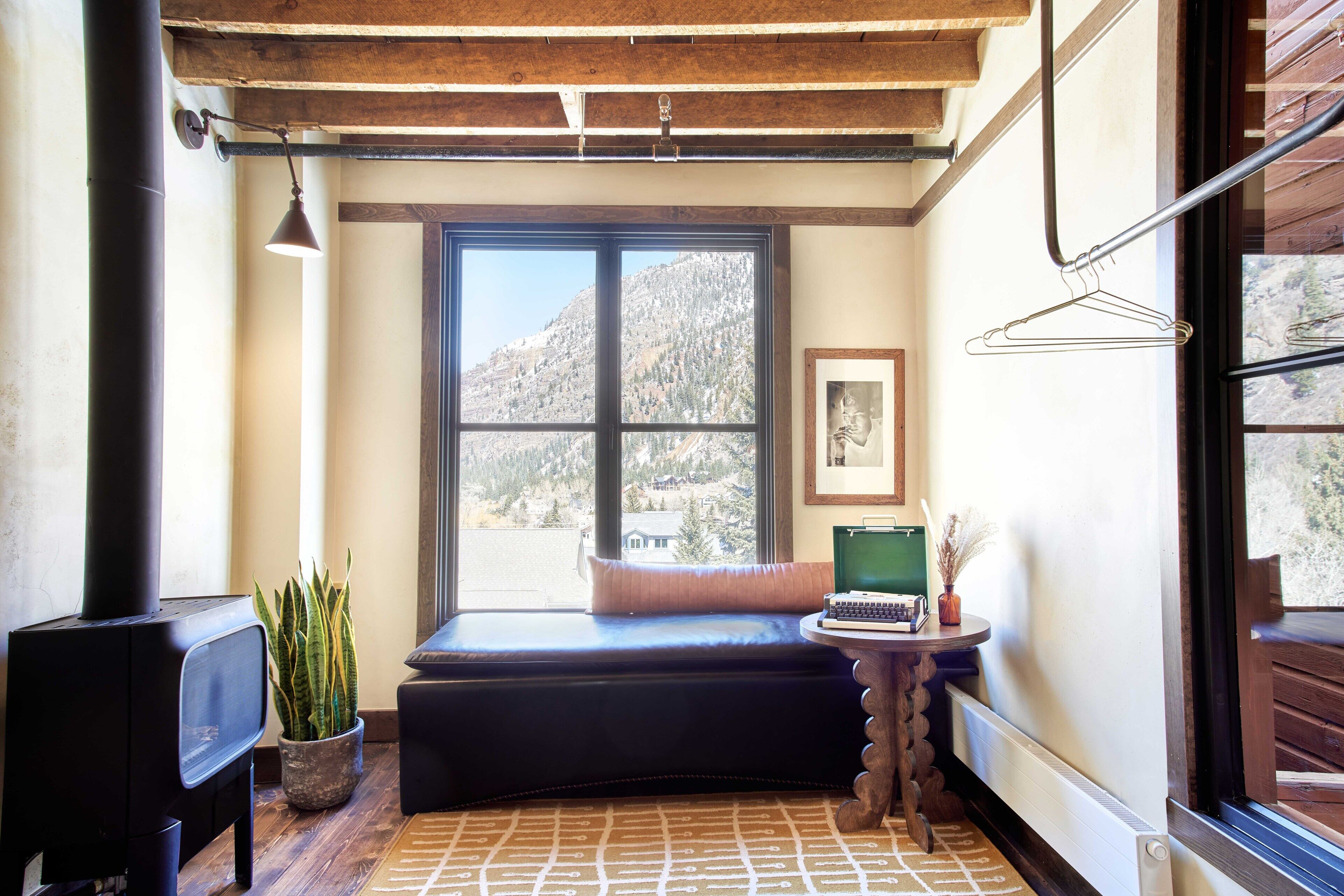 A cozy room with a large window, a black sofa, a small table with a book and a vase, and a potted plant.